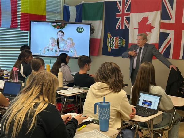  A man in a suit stands in front of a classroom of students. 